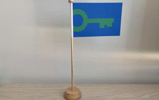 Green Key -pöytälippu puisella jalustalla seisoo puisella pöydällä. Lipussa on sininen pohja, johon on piirretty vihreä avain.