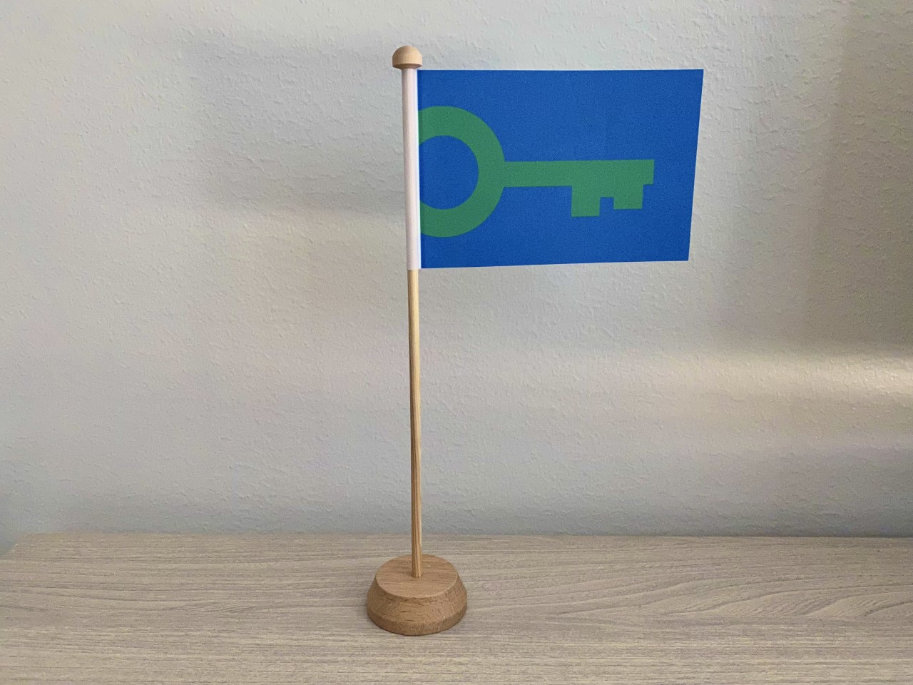Green Key -pöytälippu puisella jalustalla seisoo puisella pöydällä. Lipussa on sininen pohja, johon on piirretty vihreä avain.