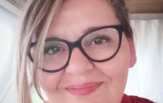 Minna-Maria Mäenpää lähikuvassa, jossa näkyvät iloiset kasvot ja hieman punaisesta paidasta.