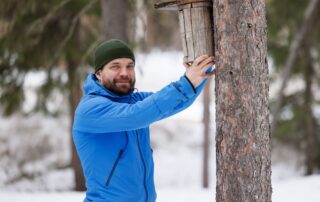 Kuvassa Mikko Äijälä ripustaa linninpönttöä talvisessa maisemassa.