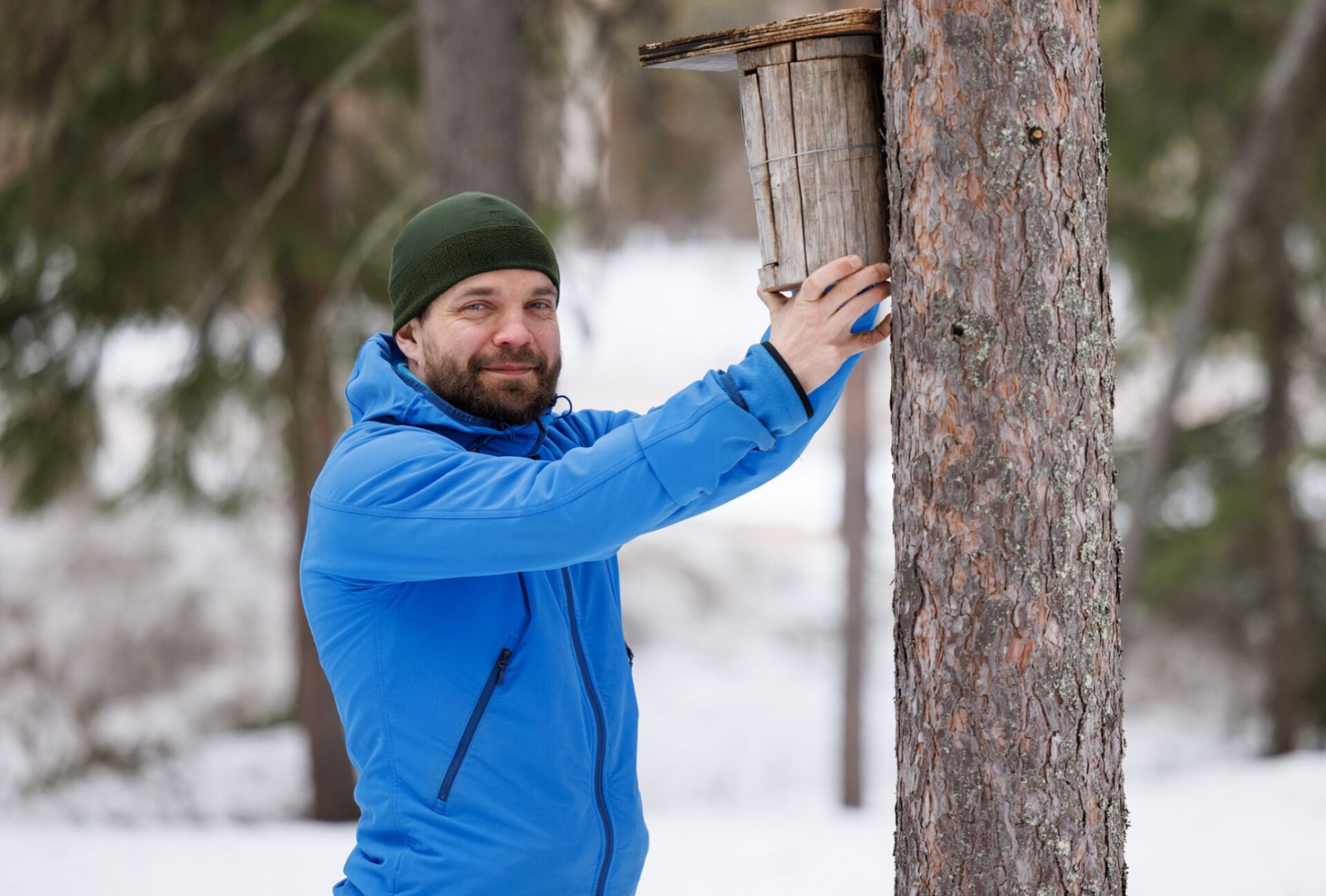 Kuvassa Mikko Äijälä ripustaa linninpönttöä talvisessa maisemassa.