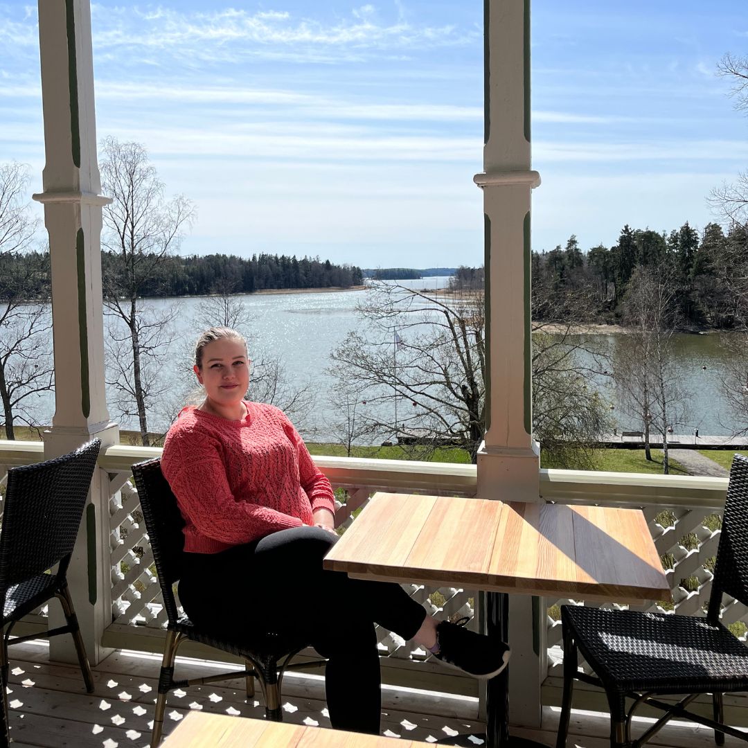 Villa Wolaxin palvelupäällikkö Milla Ahorinta istuu terassilla pöydän ääressä. Taustalla näkyy mereinen saaristomaisema.