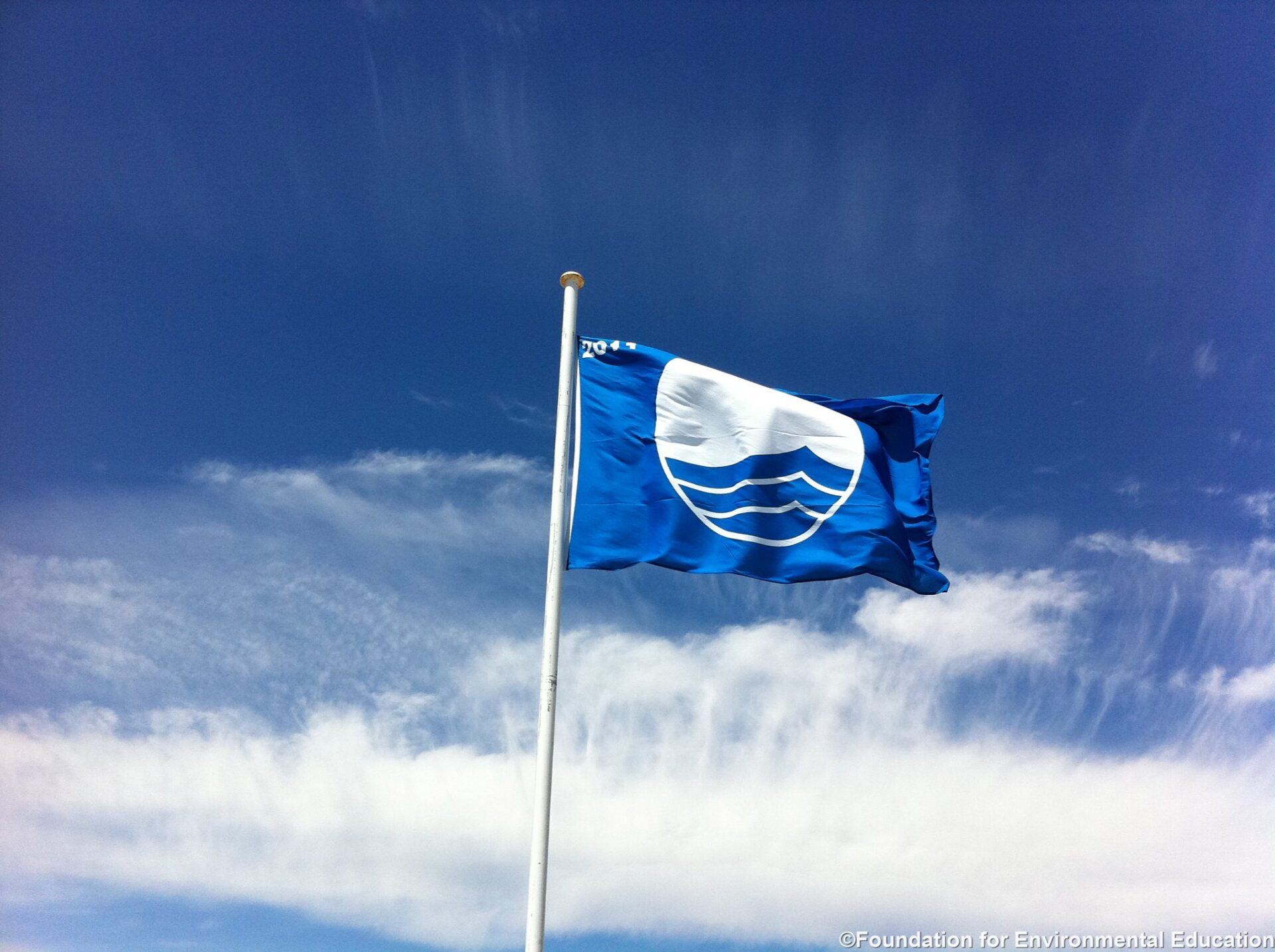 Blue Flag -lippu liehuu sinistä taivasta ja valkoisia pilvenhaituvia vasten.