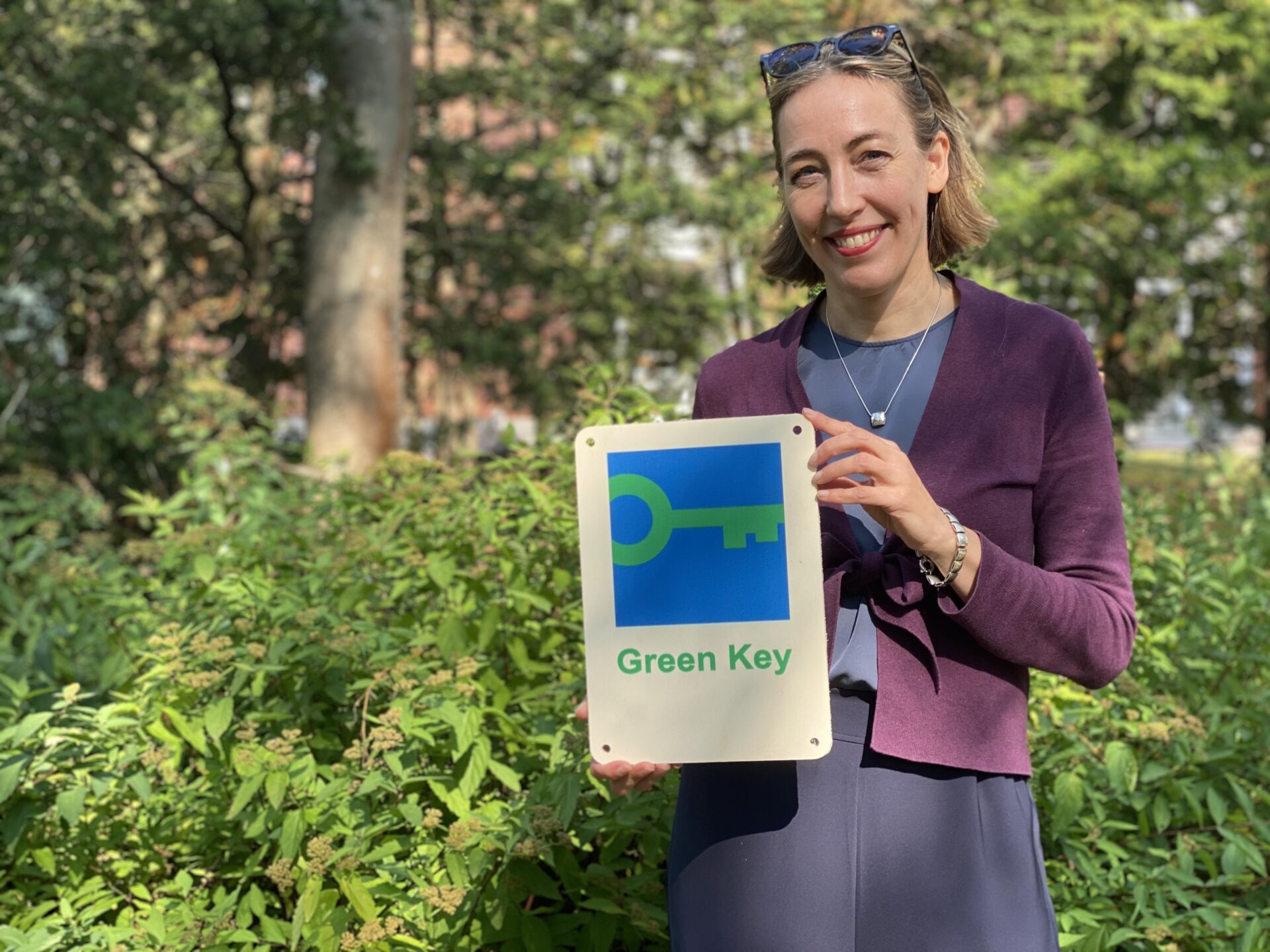 Kuvassa Heidi Heinonen poseeraa puisen Green Key -plakaatin kanssa.