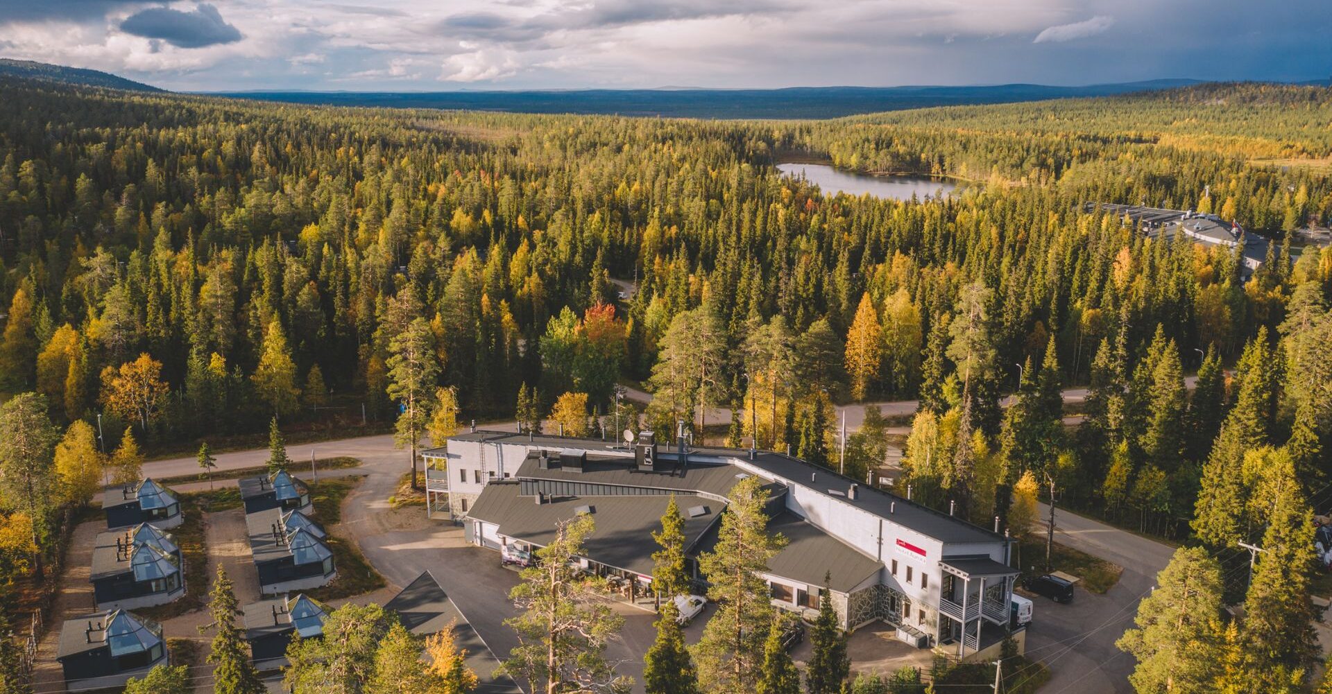 Santa's Hotel Aurora kuvattuna ilmasta käsin. Hotelli lepää ruskaisen metsän keskellä havupuiden ja keltaisten lehtipuiden syleilyssä.