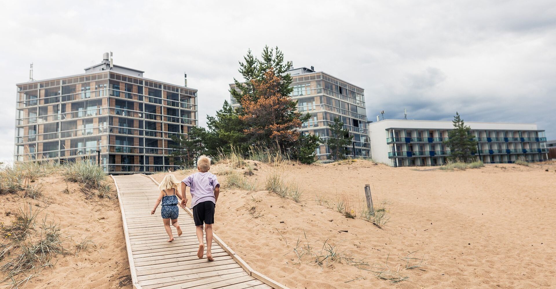 Kaksi lasta kävelee pitkospuita pitkin Kalajoen hiekoilla kohti hotellia.