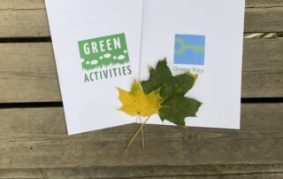 Green Key ja Green Activities kansiot kuvattuna puisella terassilla syksyisten vaahteranlehtien kanssa.