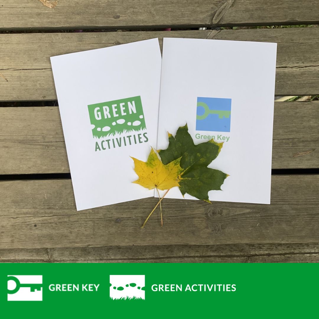Green Key ja Green Activities kansiot kuvattuna puisella terassilla syksyisten vaahteranlehtien kanssa.