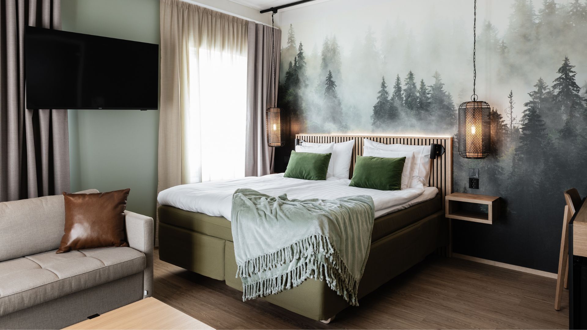 Kuvassa hotellihuone, jossa on parisänky, kaunis harmaanvihreä-sisustus ja tehosteseinänä sängyn takana metsämaisema.