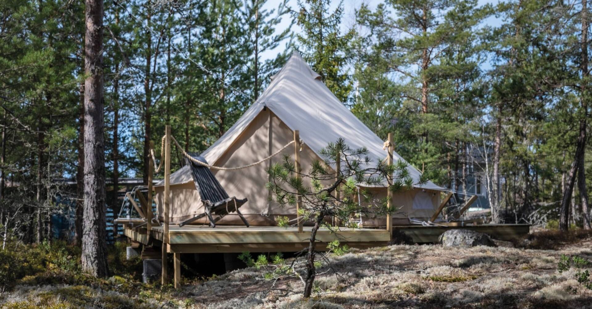 Kuusivaltaisen kallioisen metsikön keskellä terassi ja kodan tyyppinen rakennelma puusta.